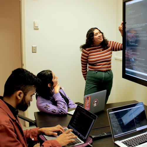 SF State professor pointing at computer screen while a class full of students watch her presentation. 