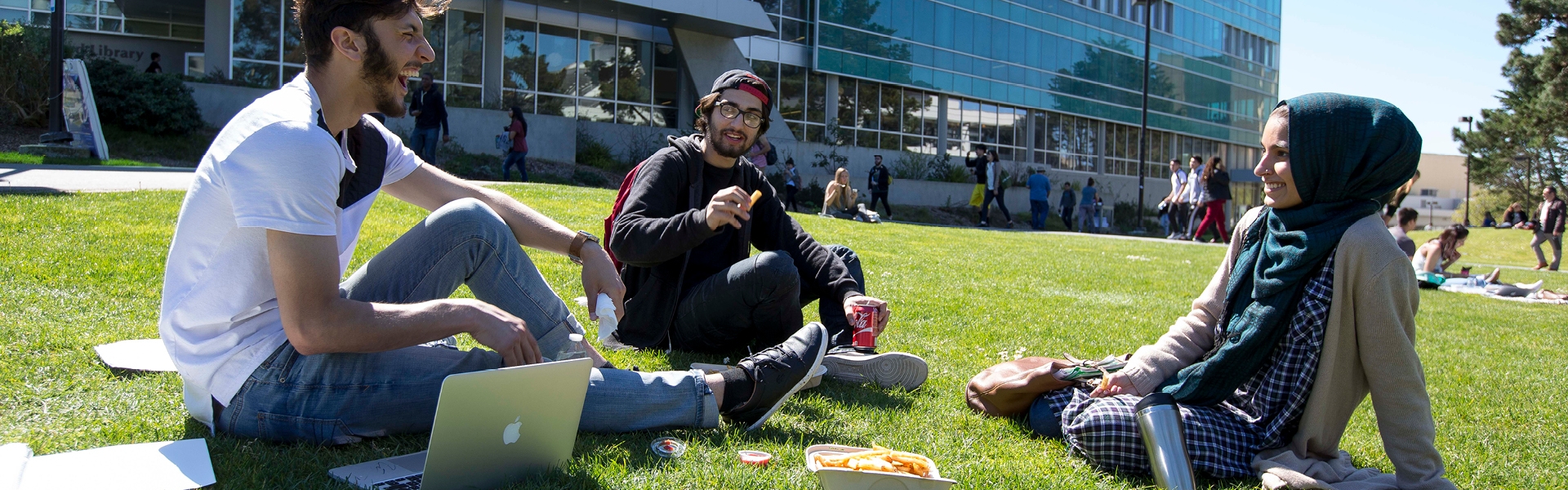 SF State student sitting on the grass in front of the library laughing