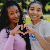 2 students making a heart next to a logo for Gator Giving Day