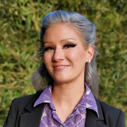 A women smiling in golden sunlight. There is blurred green foliage in the background.
