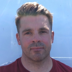 A masc presenting white person in front of a white wall